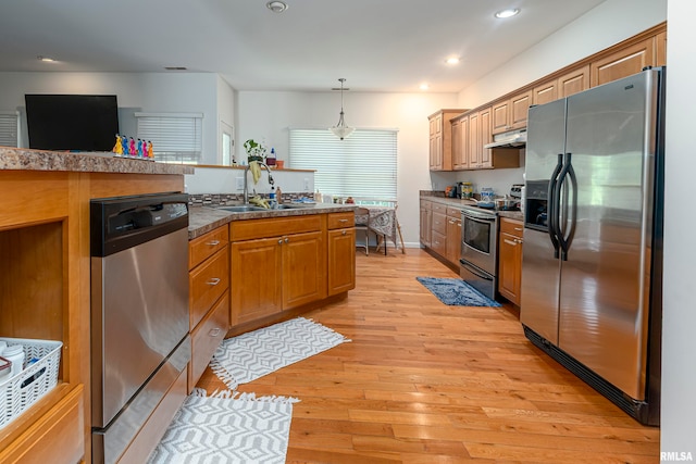 kitchen with stainless steel appliances, sink, decorative light fixtures, and light hardwood / wood-style floors