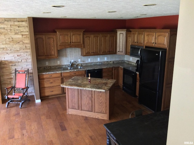 kitchen with a textured ceiling, black appliances, a kitchen island, sink, and dark wood-type flooring