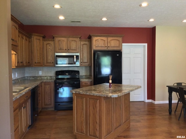 kitchen with dark hardwood / wood-style floors, black appliances, backsplash, a center island, and dark stone countertops