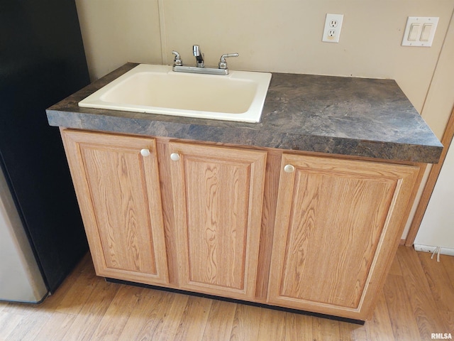 interior space with black fridge, light brown cabinetry, light hardwood / wood-style floors, and sink