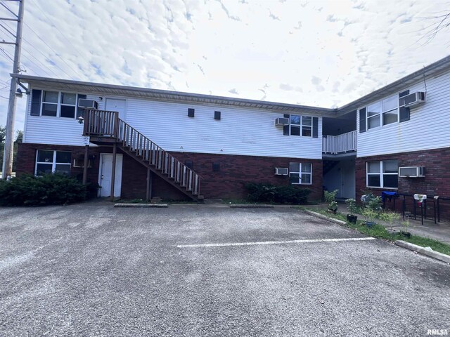 view of building exterior featuring an AC wall unit, uncovered parking, and stairway