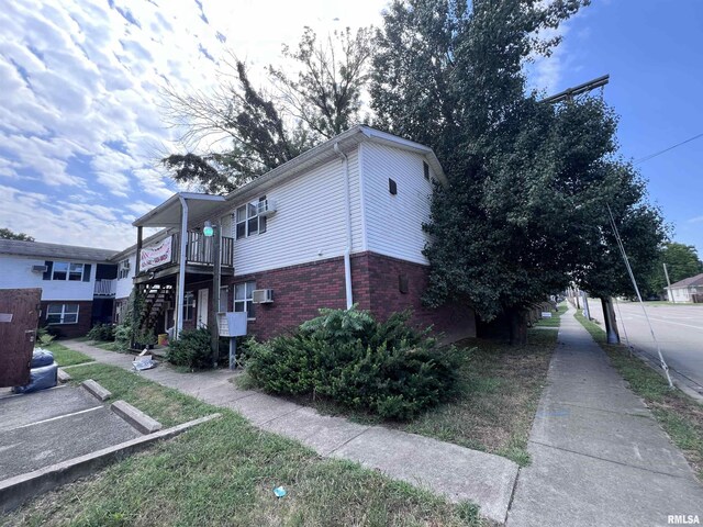 view of property exterior with uncovered parking, a wall mounted AC, brick siding, and stairway