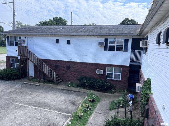 exterior space with brick siding, cooling unit, uncovered parking, and stairway