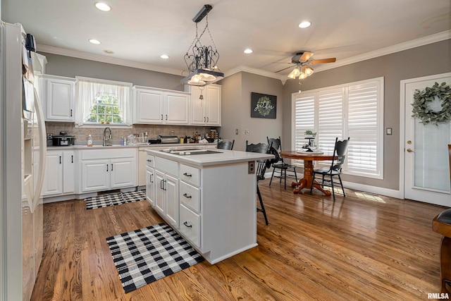 kitchen featuring white fridge with ice dispenser, a center island, hanging light fixtures, white cabinets, and light hardwood / wood-style floors