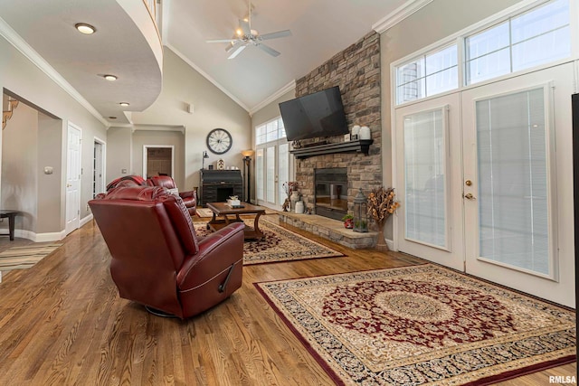 living room with hardwood / wood-style floors, a stone fireplace, ornamental molding, high vaulted ceiling, and ceiling fan