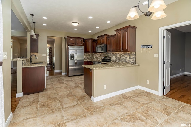 kitchen with light stone counters, a peninsula, a sink, appliances with stainless steel finishes, and tasteful backsplash