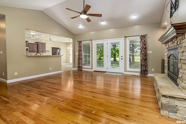 unfurnished living room with a fireplace, light wood finished floors, a ceiling fan, high vaulted ceiling, and baseboards