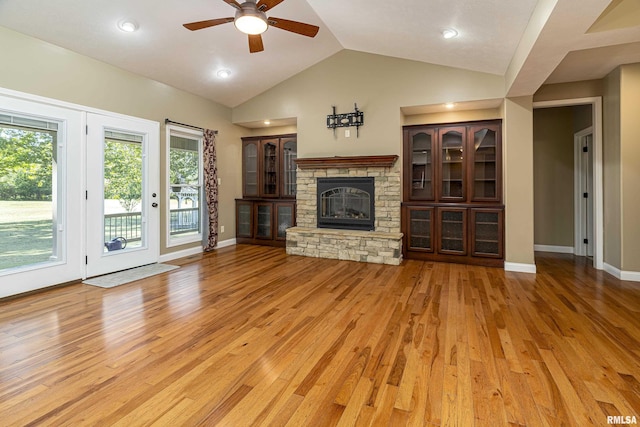 unfurnished living room with light wood-type flooring, vaulted ceiling, a stone fireplace, and ceiling fan