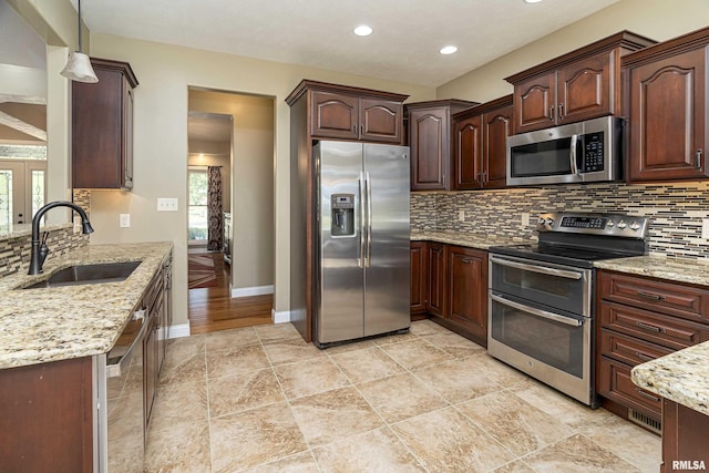 kitchen featuring baseboards, decorative backsplash, appliances with stainless steel finishes, light stone countertops, and a sink