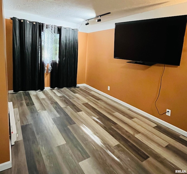 empty room with a textured ceiling, wood-type flooring, and rail lighting