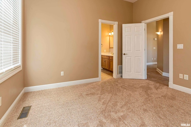 unfurnished bedroom featuring ensuite bath and light colored carpet