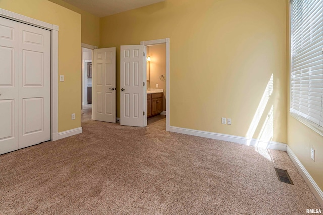 unfurnished bedroom featuring connected bathroom, light carpet, and a closet