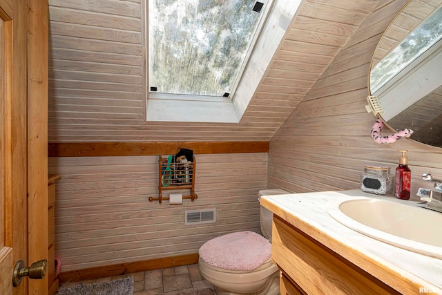 bathroom with wooden walls, lofted ceiling with skylight, vanity, and toilet