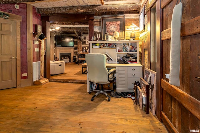 home office featuring light wood-type flooring, wooden walls, and beamed ceiling