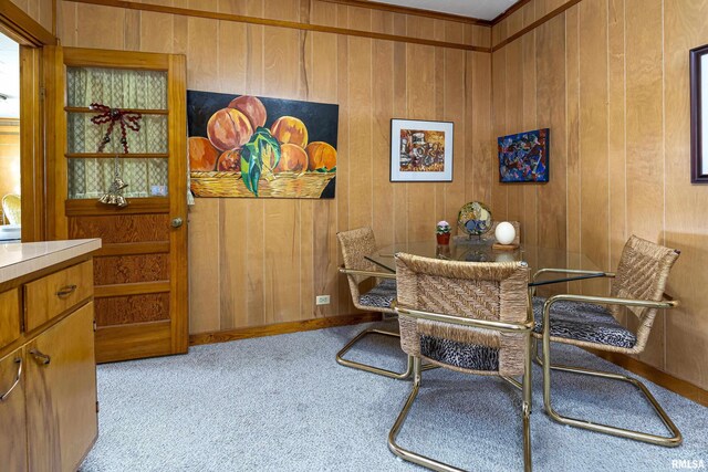 dining space featuring wood walls, light colored carpet, and crown molding