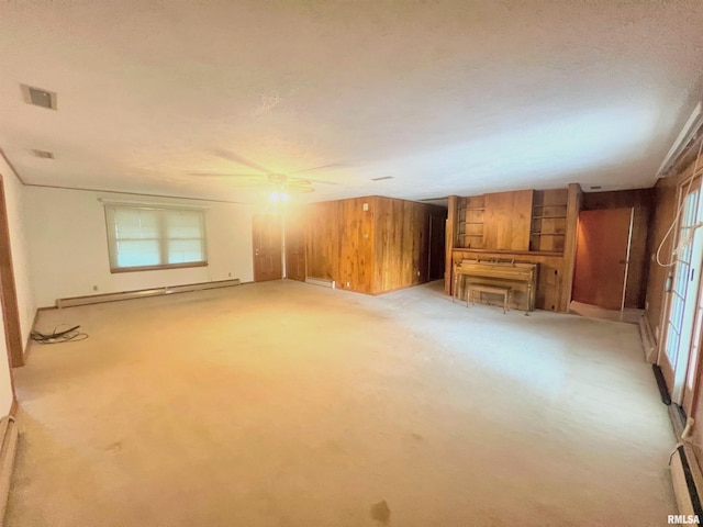 unfurnished living room with wood walls, ceiling fan, light colored carpet, and a healthy amount of sunlight