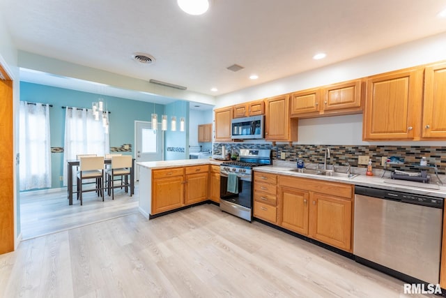 kitchen with pendant lighting, sink, kitchen peninsula, light hardwood / wood-style flooring, and stainless steel appliances