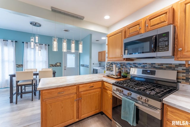 kitchen with light hardwood / wood-style floors, kitchen peninsula, pendant lighting, stainless steel appliances, and washer and clothes dryer