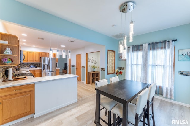 kitchen with light wood-type flooring, stainless steel refrigerator with ice dispenser, kitchen peninsula, and decorative light fixtures