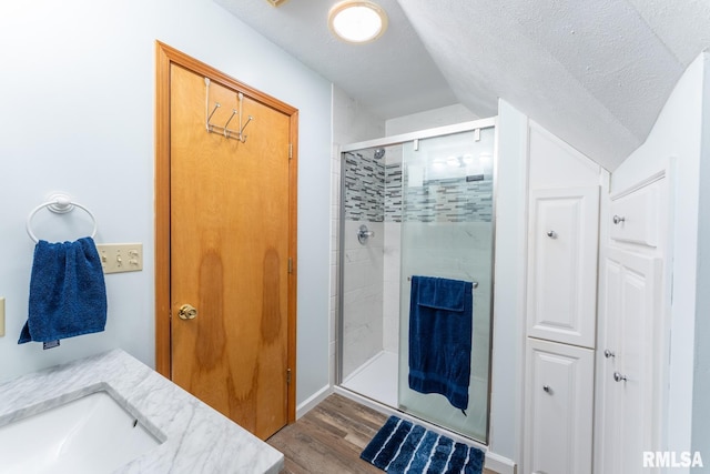 bathroom featuring vaulted ceiling, vanity, a textured ceiling, wood-type flooring, and an enclosed shower