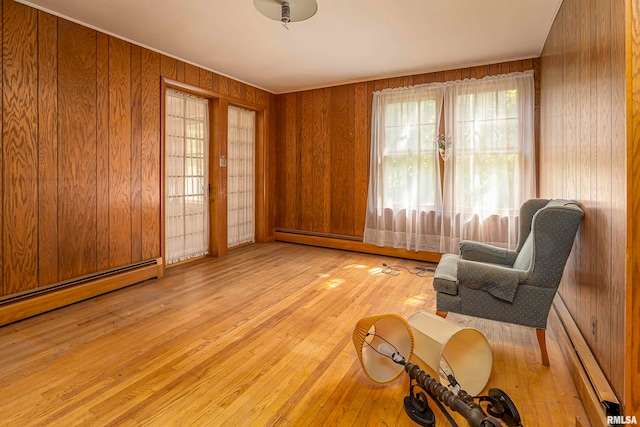 unfurnished room featuring light hardwood / wood-style floors, wood walls, and a baseboard radiator