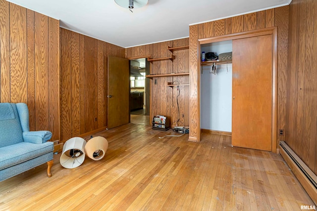 unfurnished room with light wood-type flooring, wooden walls, and a baseboard heating unit