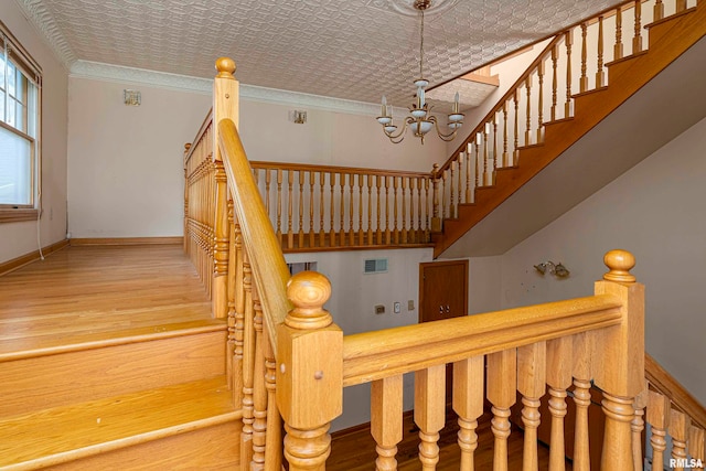 staircase featuring an inviting chandelier, a textured ceiling, ornamental molding, and hardwood / wood-style floors