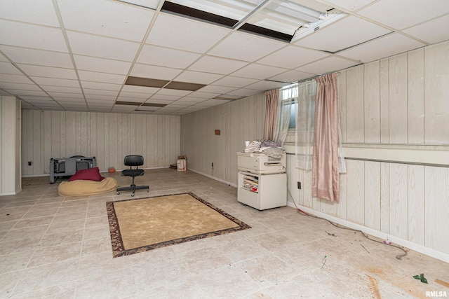 basement featuring a drop ceiling and wooden walls