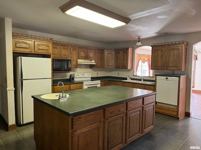 kitchen featuring sink, white appliances, dark tile patterned floors, and a center island with sink