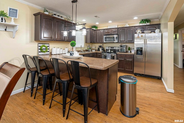 kitchen with light hardwood / wood-style flooring, appliances with stainless steel finishes, dark brown cabinets, a kitchen bar, and kitchen peninsula