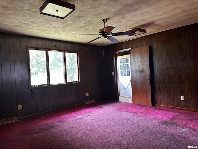 carpeted spare room with ceiling fan, a textured ceiling, and wood walls