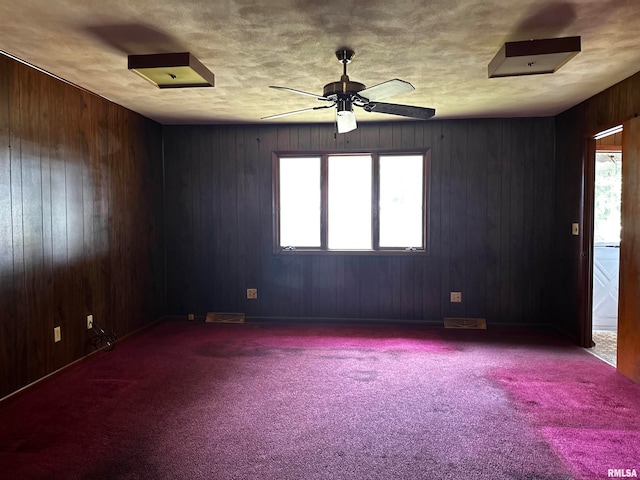 carpeted empty room featuring wood walls and ceiling fan