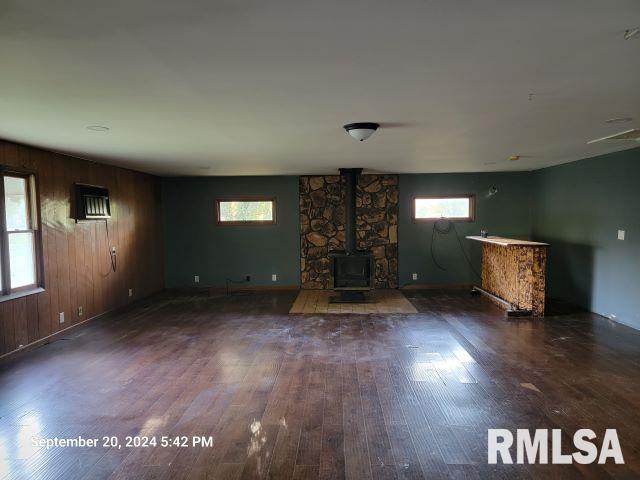 unfurnished living room featuring a healthy amount of sunlight, dark hardwood / wood-style flooring, and a wood stove