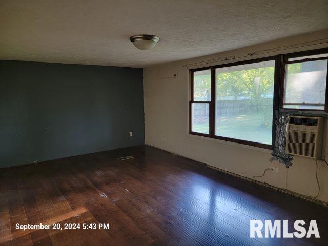 empty room featuring cooling unit, a textured ceiling, and dark hardwood / wood-style flooring