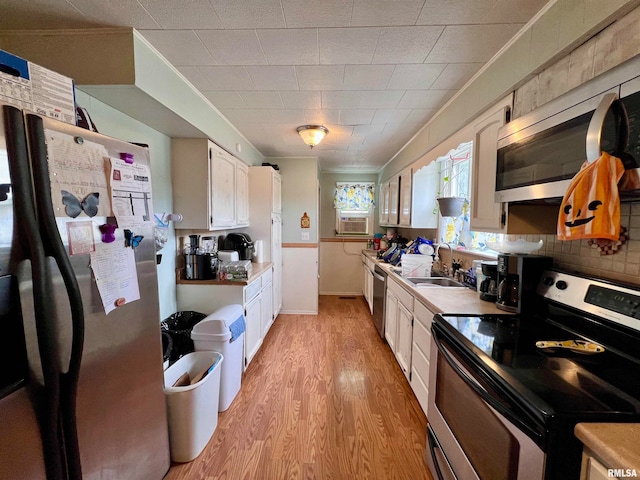 kitchen with appliances with stainless steel finishes, white cabinets, light hardwood / wood-style flooring, ornamental molding, and sink