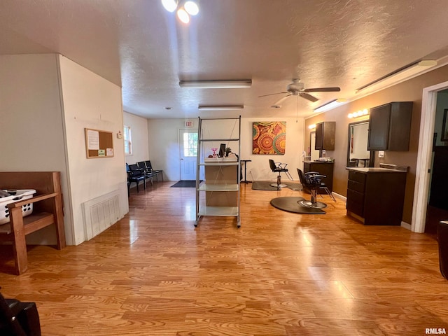 interior space with a textured ceiling, ceiling fan, and light hardwood / wood-style flooring