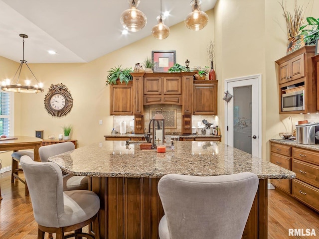 kitchen featuring stainless steel microwave, pendant lighting, light hardwood / wood-style flooring, a kitchen island with sink, and a chandelier