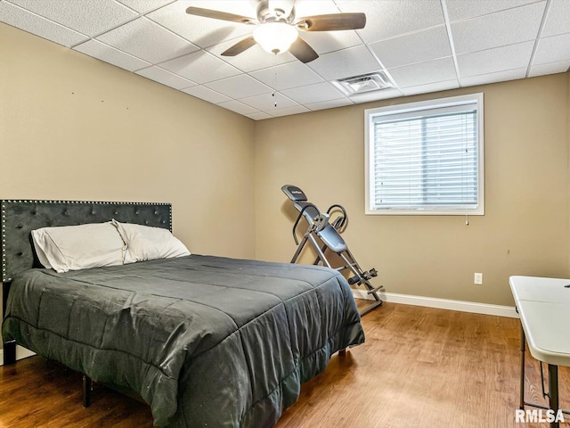 bedroom featuring ceiling fan, a drop ceiling, and wood-type flooring