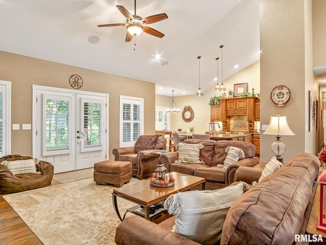 living room featuring ceiling fan with notable chandelier, light wood-type flooring, high vaulted ceiling, and french doors