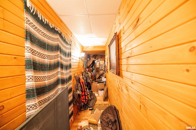 hall with a paneled ceiling, wooden walls, and wood finished floors