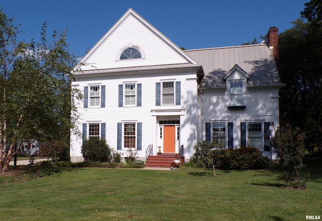 greek revival inspired property featuring metal roof, a front yard, a standing seam roof, and a chimney