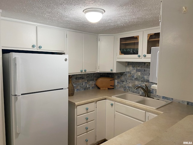 kitchen with white refrigerator, sink, a textured ceiling, backsplash, and white cabinetry