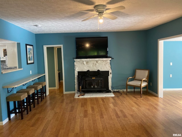 sitting room featuring ceiling fan, a stone fireplace, a textured ceiling, and wood-type flooring