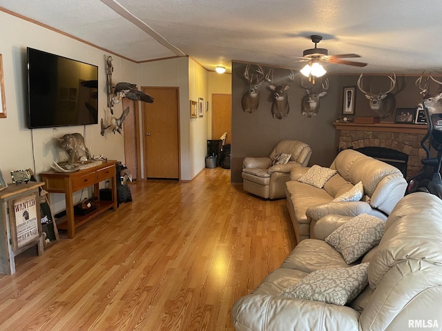 living room featuring a fireplace, light wood-type flooring, crown molding, a textured ceiling, and ceiling fan