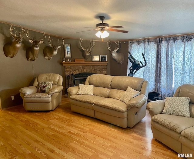 living room featuring ceiling fan, light hardwood / wood-style floors, a fireplace, and a textured ceiling