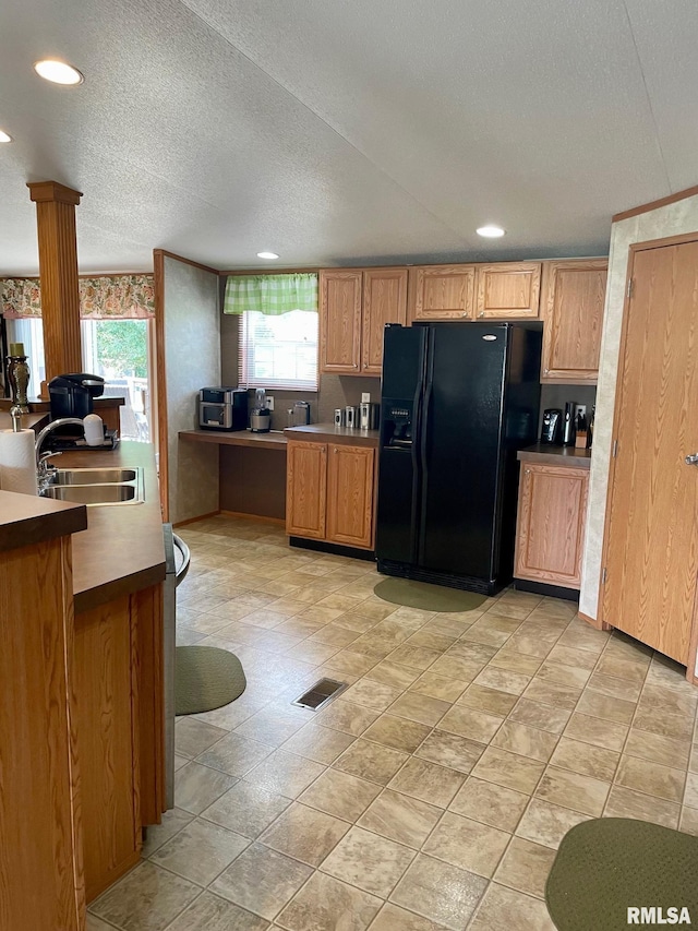 kitchen featuring a textured ceiling, decorative columns, sink, and black fridge