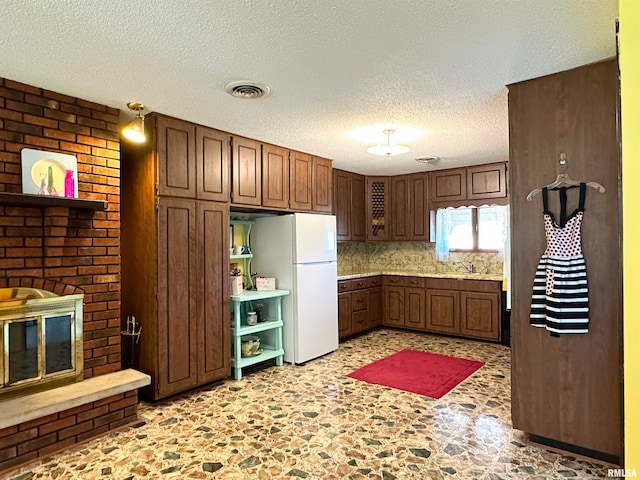 kitchen featuring white refrigerator, a textured ceiling, sink, a brick fireplace, and backsplash