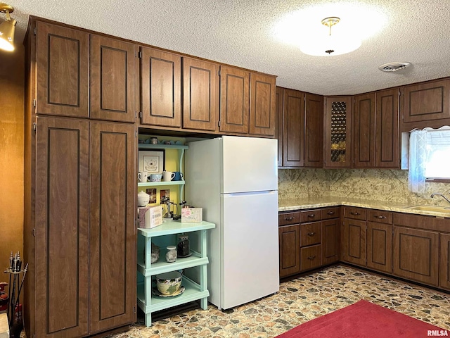 kitchen featuring decorative backsplash, a textured ceiling, white fridge, and sink