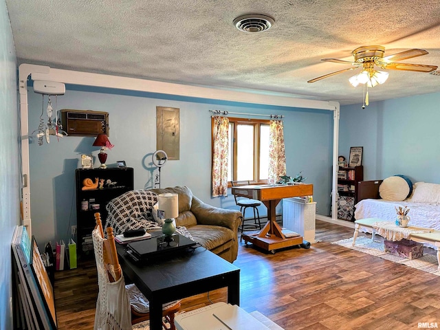 living room featuring a textured ceiling, electric panel, an AC wall unit, dark hardwood / wood-style flooring, and ceiling fan