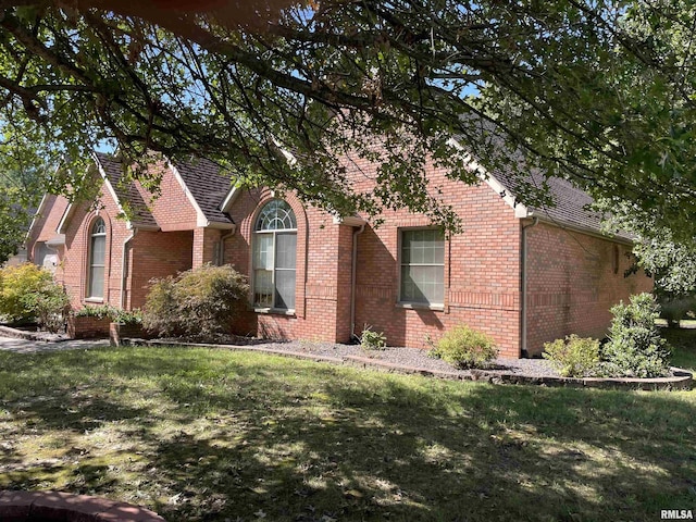 view of property hidden behind natural elements featuring brick siding, a front lawn, and roof with shingles